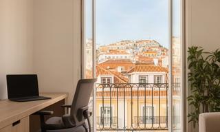 Bright furnished Lisbon apartment with a desk beside a balcony and city rooftops