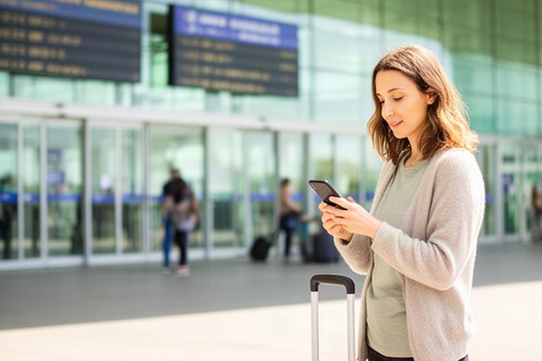 Remote worker with carry-on luggage checking arrival details outside a bright European airport